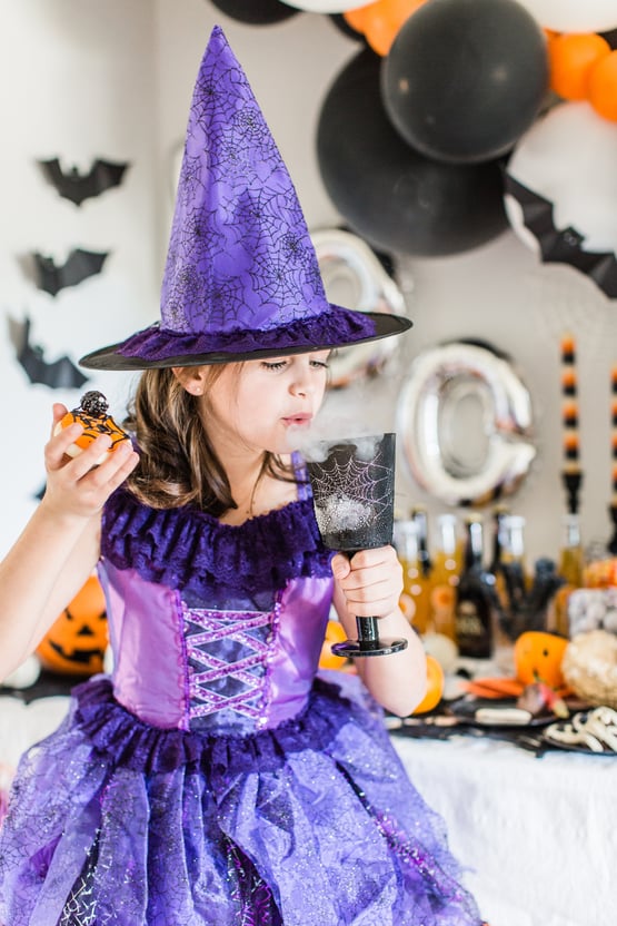 a child dressed up as a witch holding a cookie and a spiderweb glass