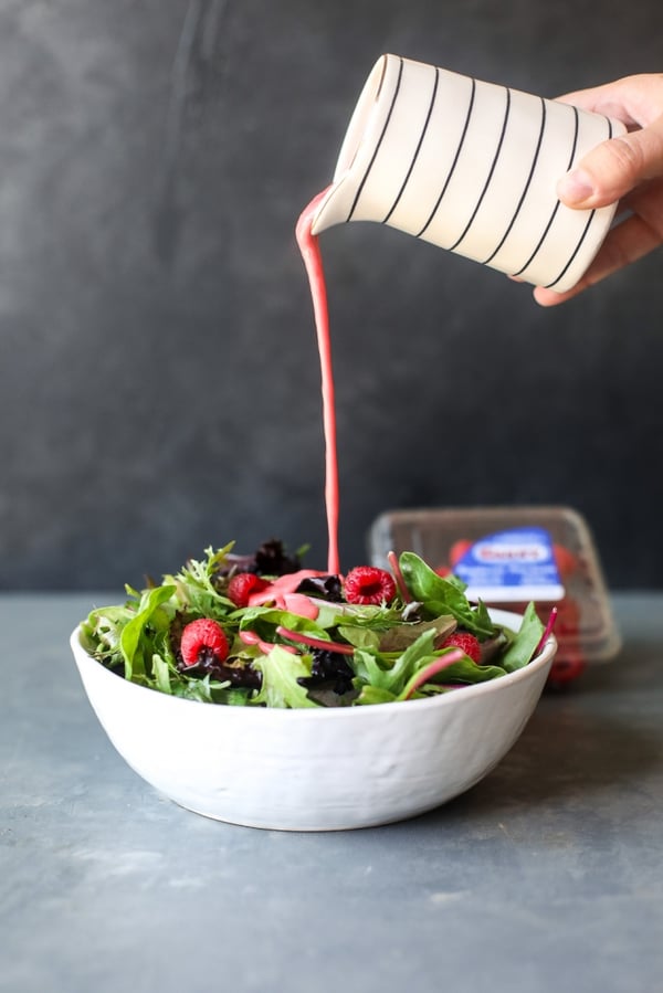 raspberry vinnagrete being poured onto a salad that is topped with raspberries
