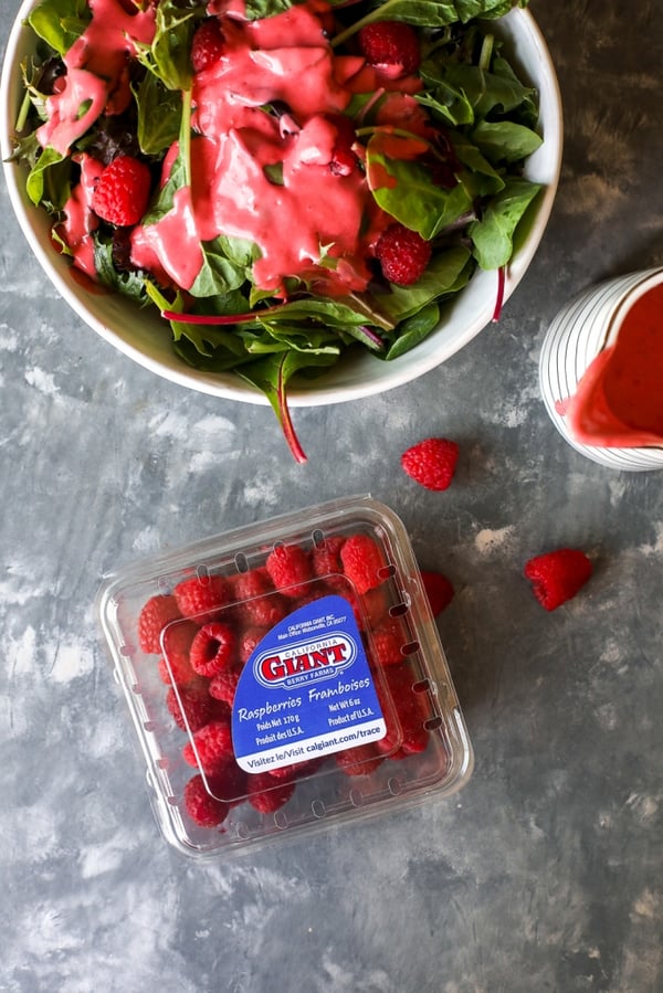 a salad topped with raspberry vinaigrette and a raspberry clamshell on the side