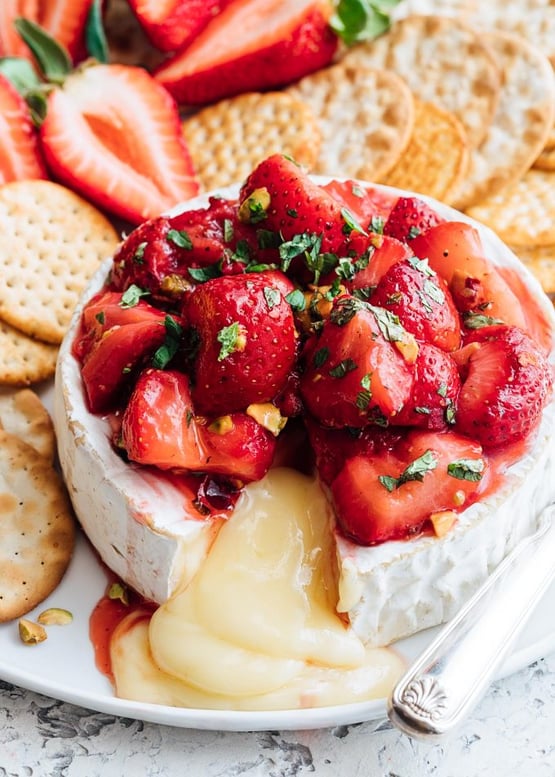 baked brie topped with roasted strawberries with a side of crackers