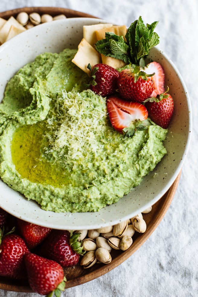 sweet pea hummus with a strawberry garnish and berries, crackers, and pistachios on the side