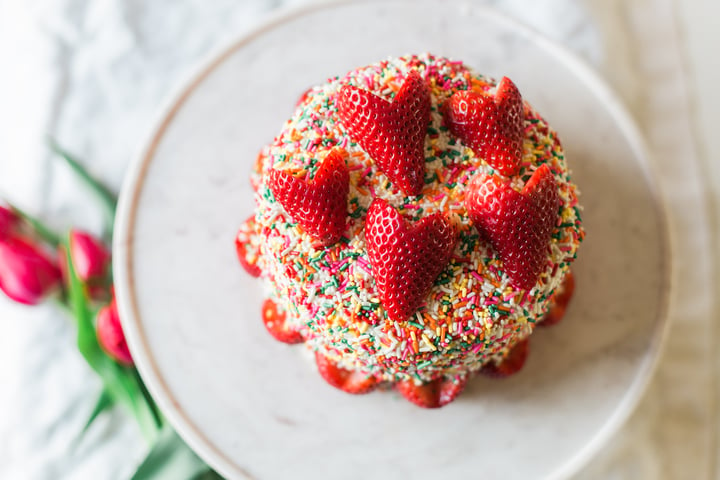 cake covered in rainbow sprinkles topped with strawberries cut like hearts