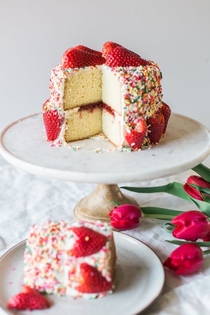 a sliced cake covered in rainbow sprinkles topped with strawberries cut like hearts