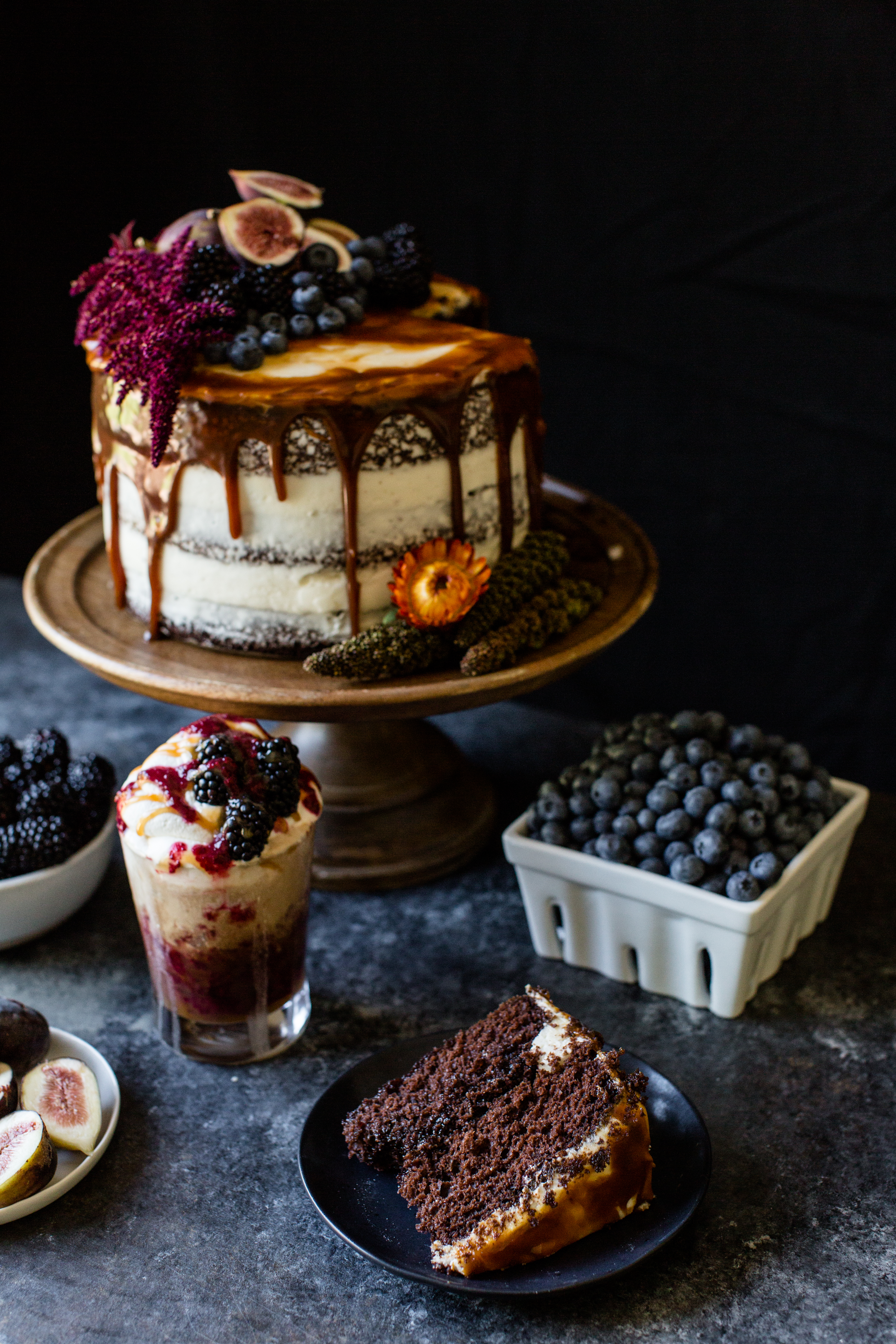 a cake on a stand with a slice in front of it and a clamshell of blueberries on the side.