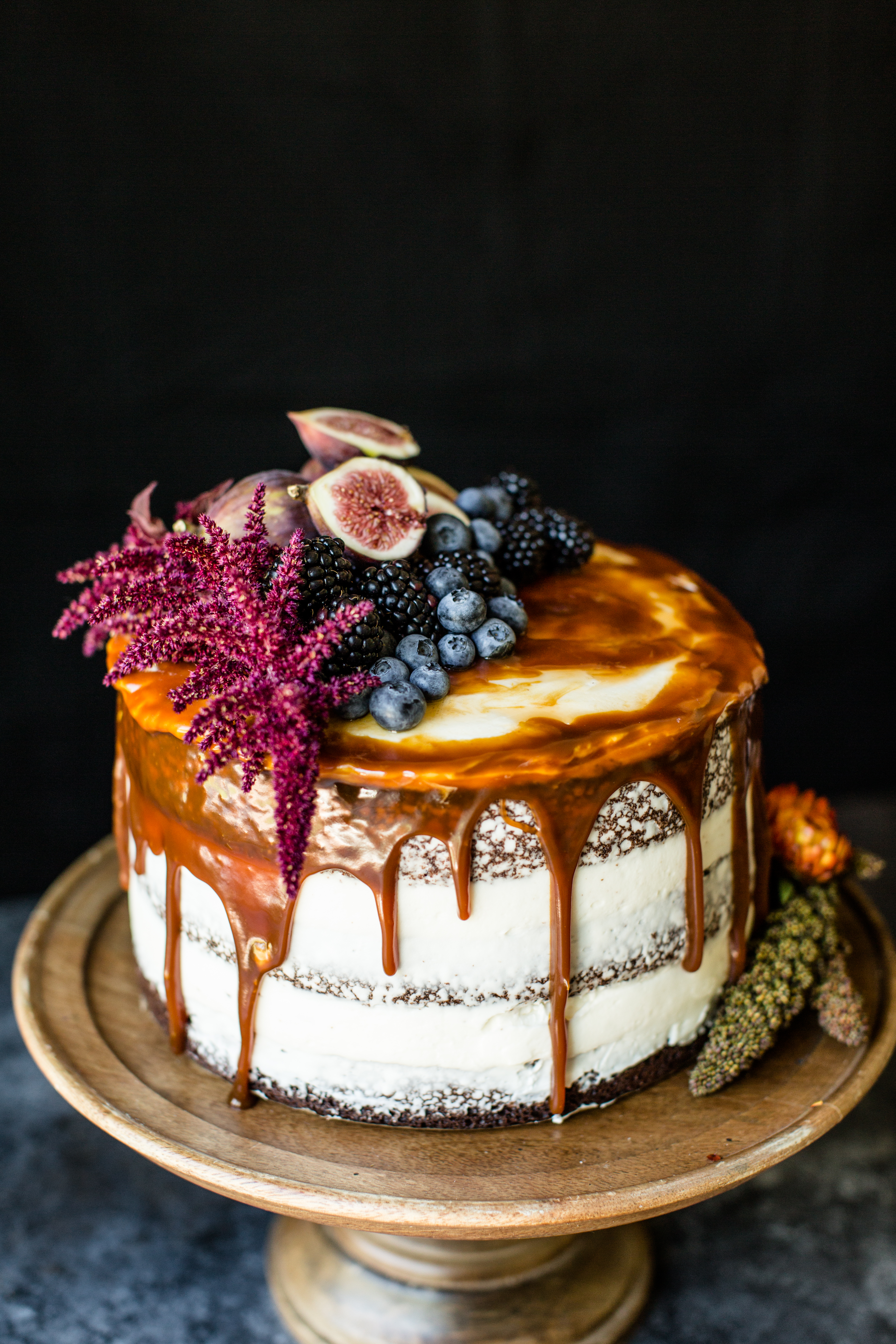 a round cake that is topped with caramel, blackberries, blueberries, and figs
